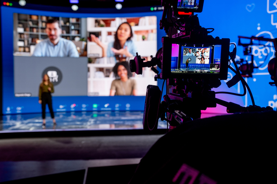 Cinema camera monitor framing a presenter on stage in front of a large video wall during an event rehearsal