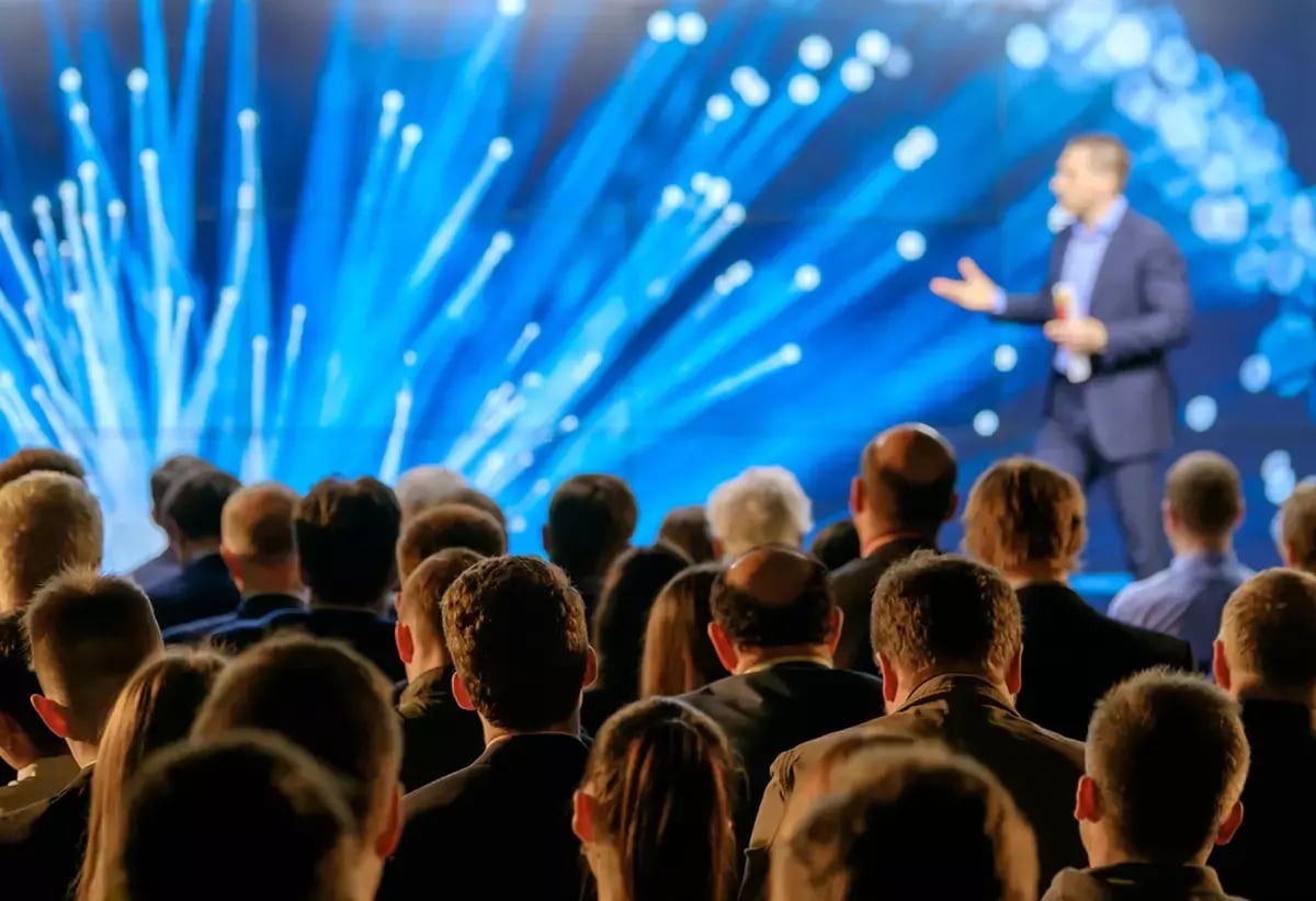 A crowd watching a man present at a corporate event.