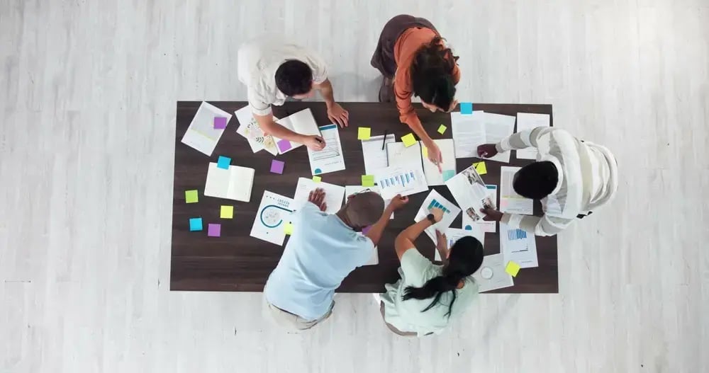 An event planning team gathered aropund a table covered in paper and notes.