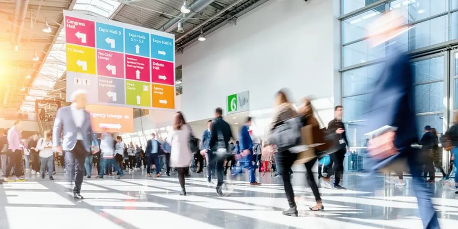 A blurred photo of people walking through a convention center.