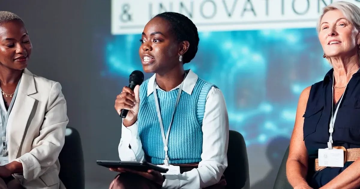 Three women speaking on a panel discussion at a corporate event.