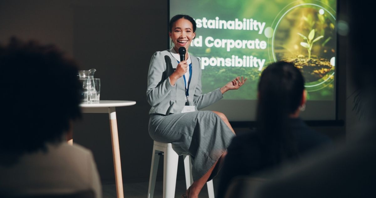 A businesswoman sitting on a stage, speaking at a corporate event about sustainability and corporate responsibility.