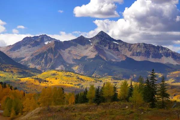 Snow-dusted Colorado mountain peaks above golden aspen trees on an autumn day