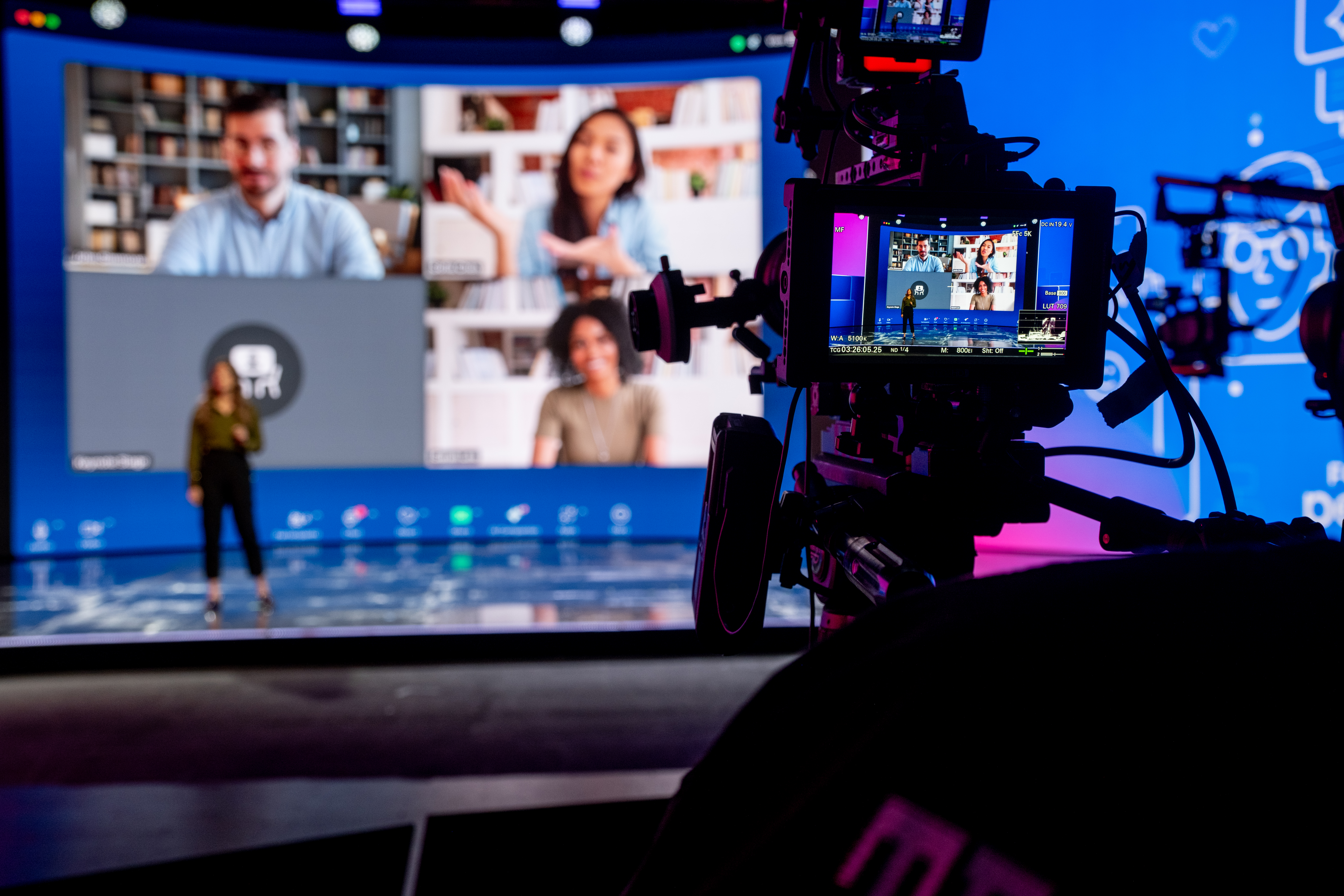 Cinema camera monitor framing a presenter on stage in front of a large video wall during an event rehearsal